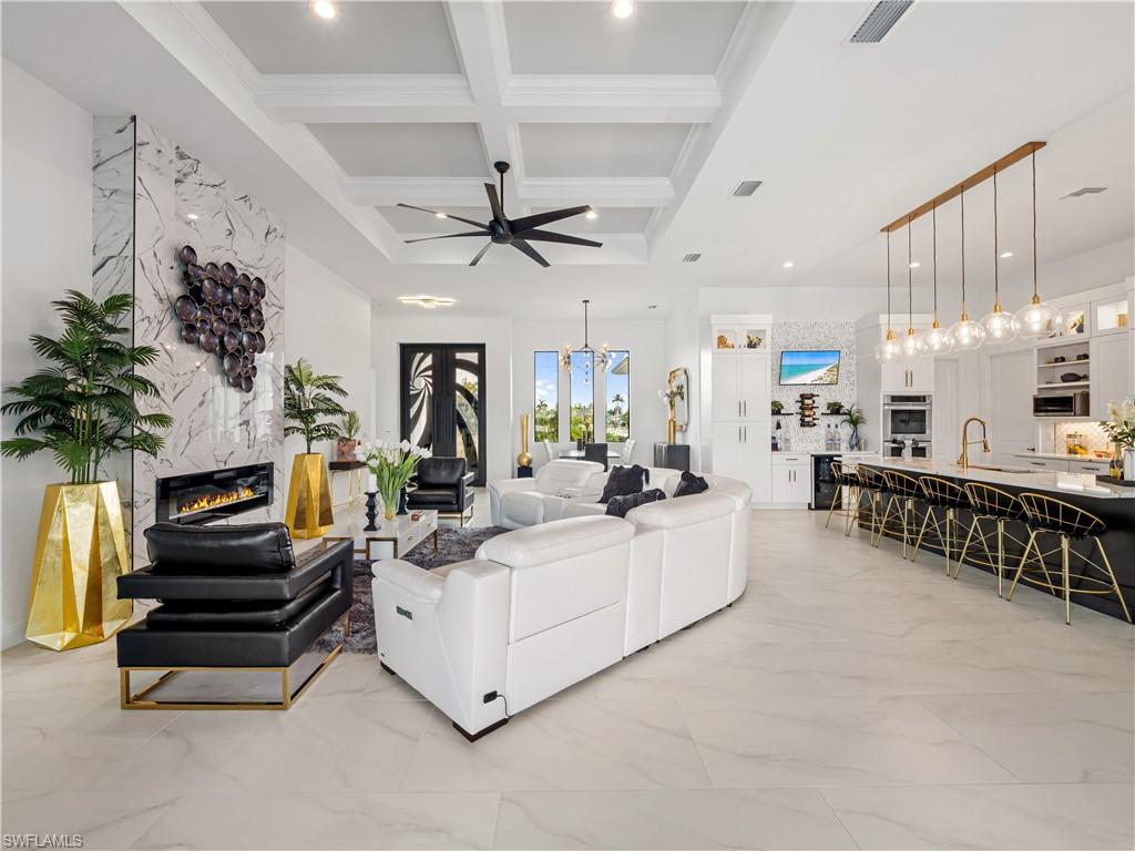 Living area with hanging lights, light marble finish flooring, coffered ceiling, a fireplace, and a ceiling fan