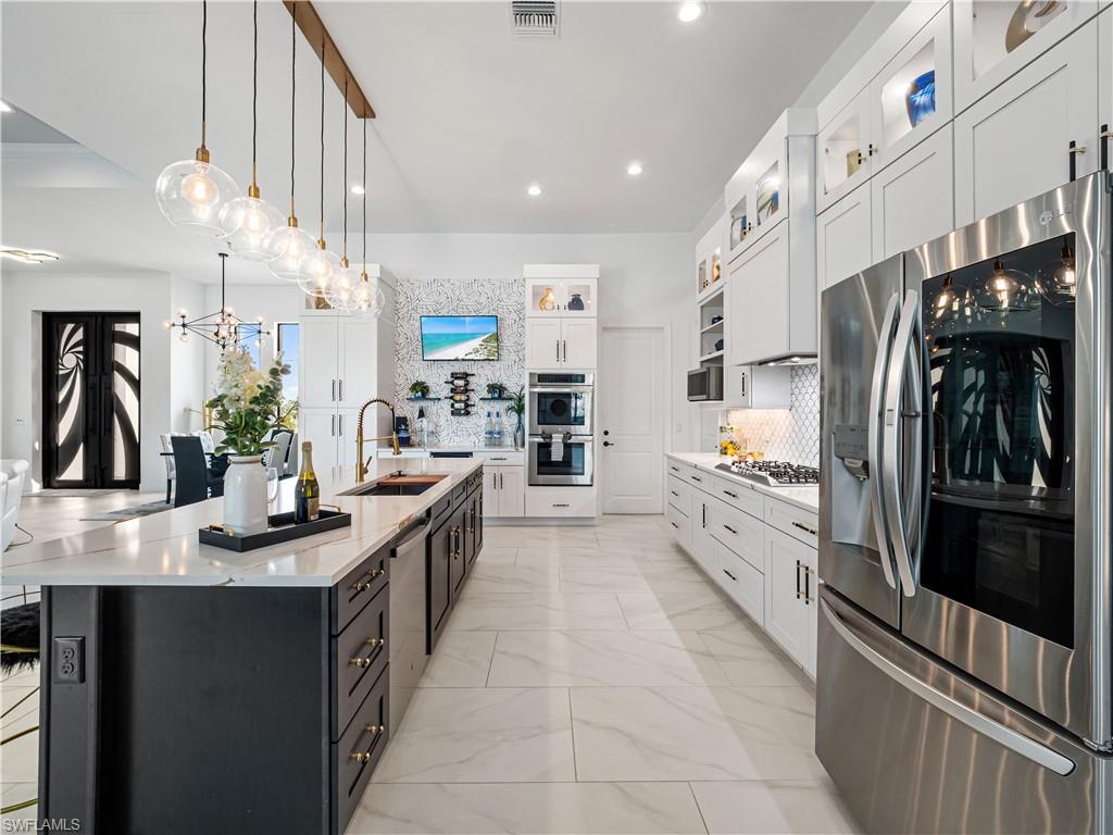 Kitchen with stainless steel appliances, two tone cabinetry, light stone counters, pendant lighting, and backsplash