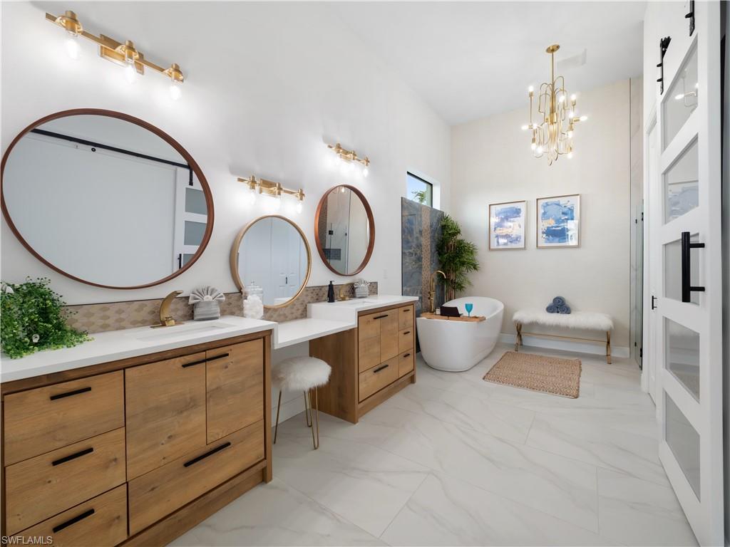 Bathroom with double vanity, a freestanding bath, light marble finish floors, and hanging lights