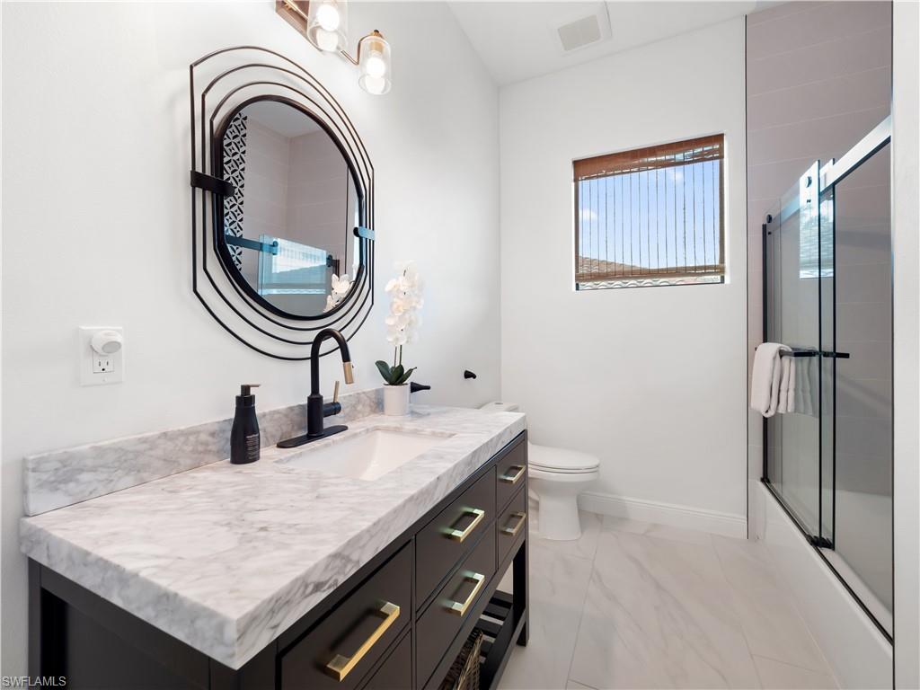 Full bath featuring vanity, bath / shower combo with glass door, and light marble finish floors