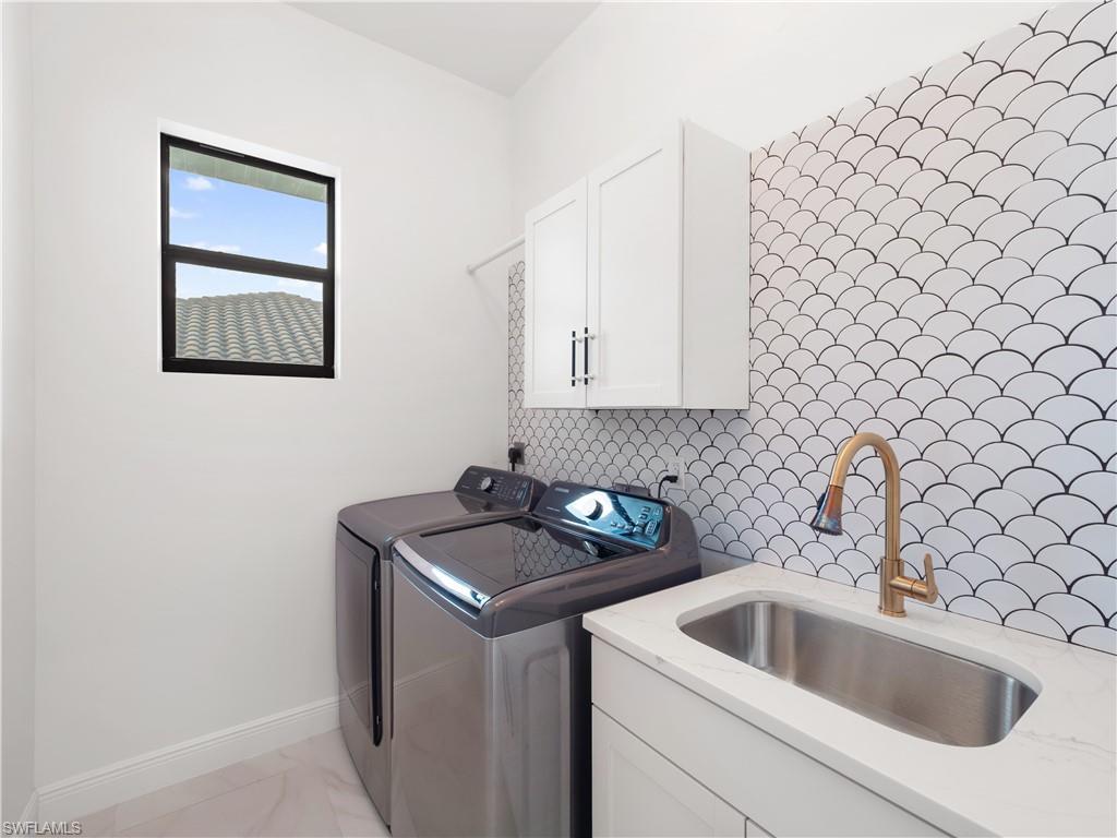 Laundry room featuring cabinet space, washing machine and clothes dryer, and light marble finish flooring