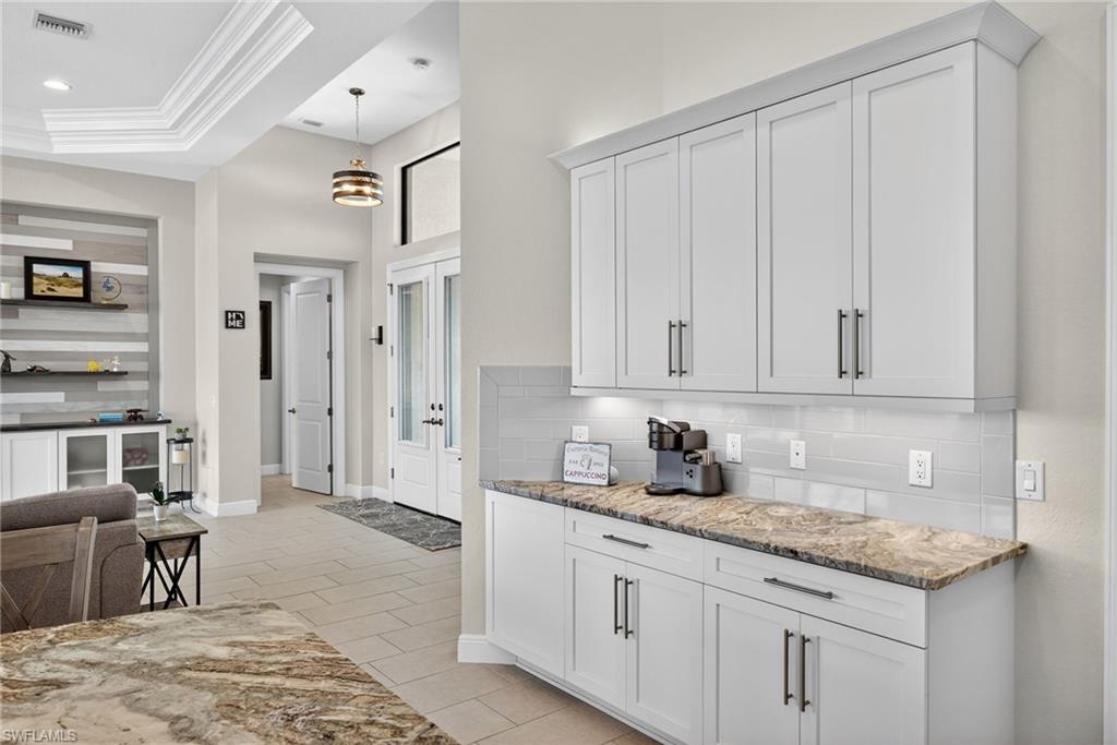Kitchen featuring light stone countertops, white cabinets, crown molding, and a tray ceiling