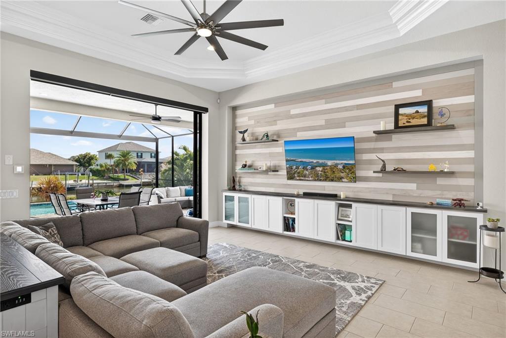 Living area custom entertainment wall, crown molding, a ceiling fan, and a tray ceiling