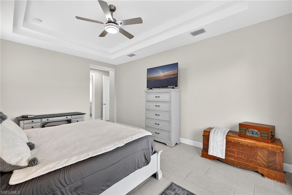 Primary bedroom with access to outside, ceiling fan, a tray ceiling, and light tile patterned flooring