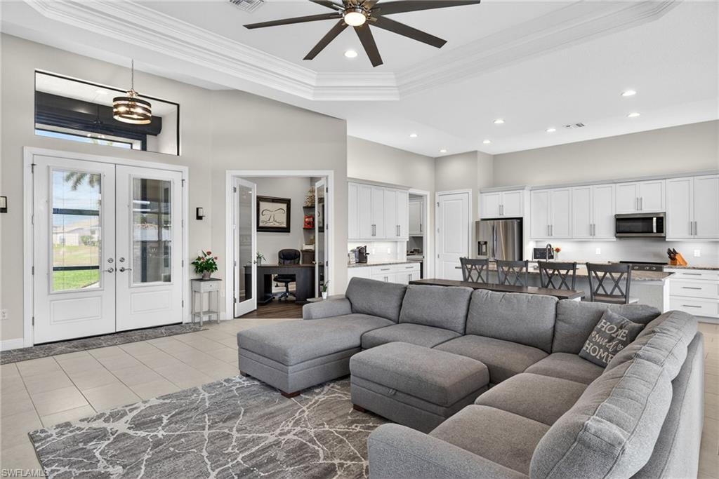 Living room with french doors, ornamental molding, ceiling fan, a tray ceiling, and suspended lighting.