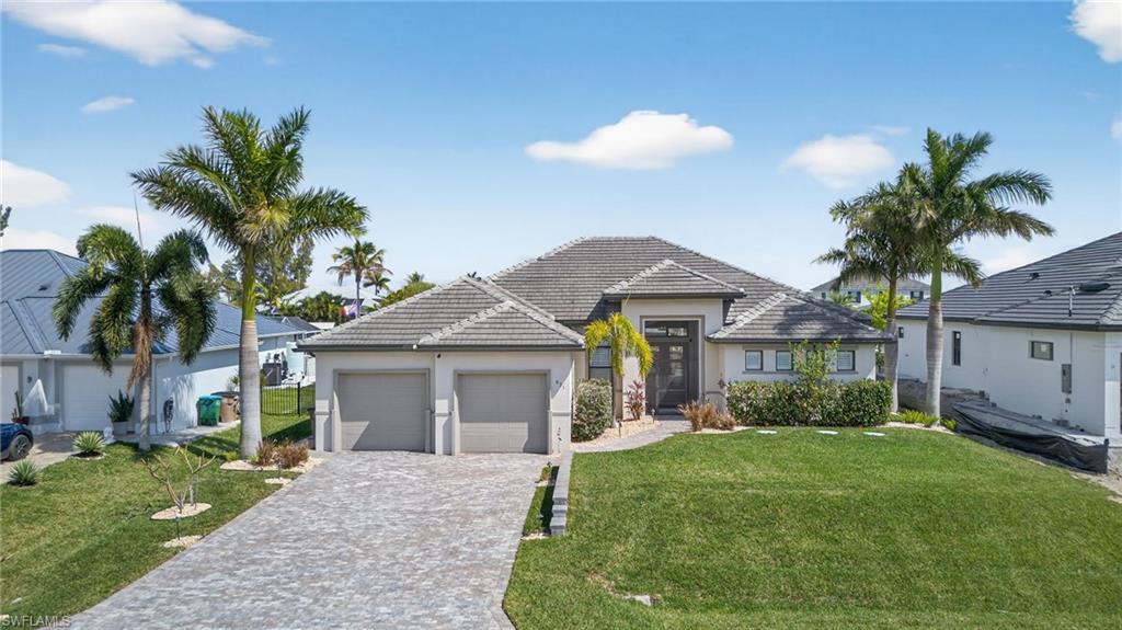 View of front of property featuring a front yard, decorative driveway, a garage, stucco siding, and a tile roof