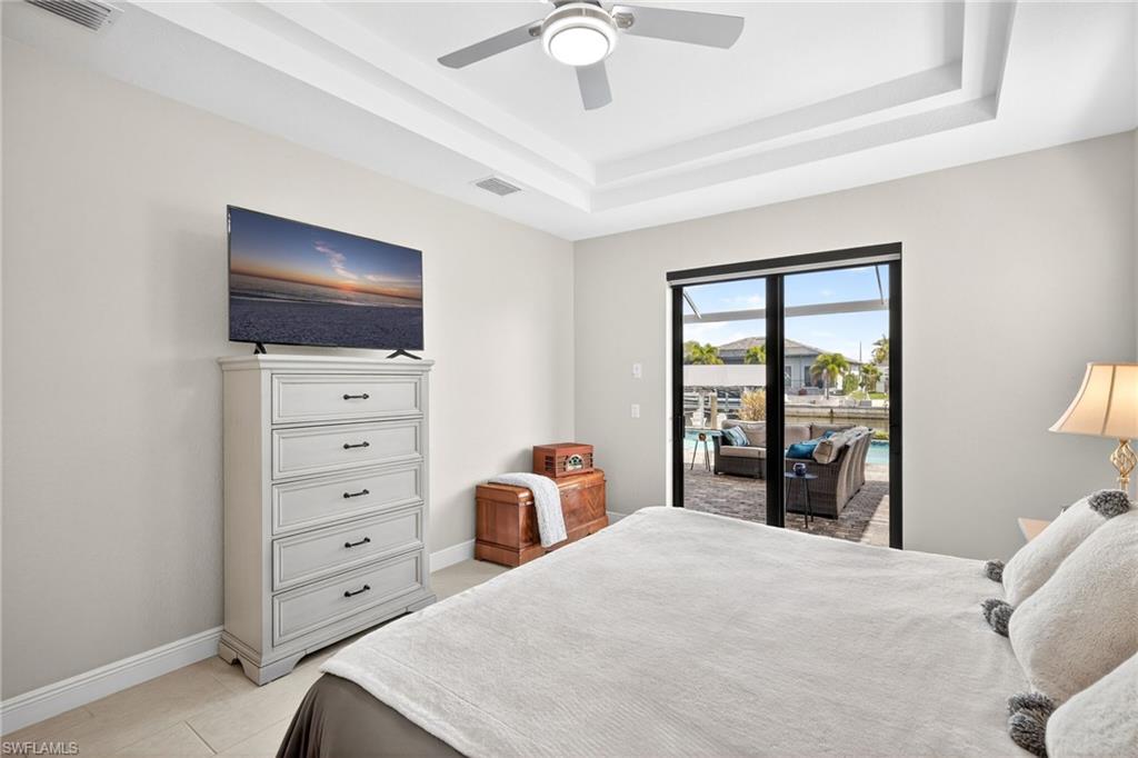 Primary bedroom with access to outside, ceiling fan, a tray ceiling, and light tile patterned flooring