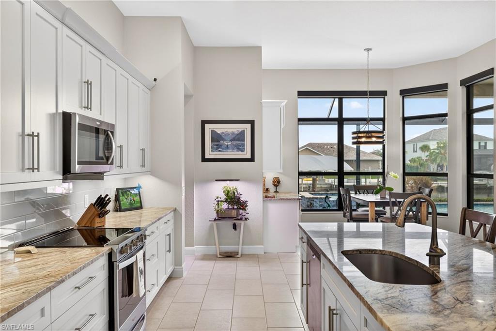 Kitchen with stainless steel appliances, a breakfast bar, light stone countertops, an island with sink, and white cabinets with under and upper cabinet lighting