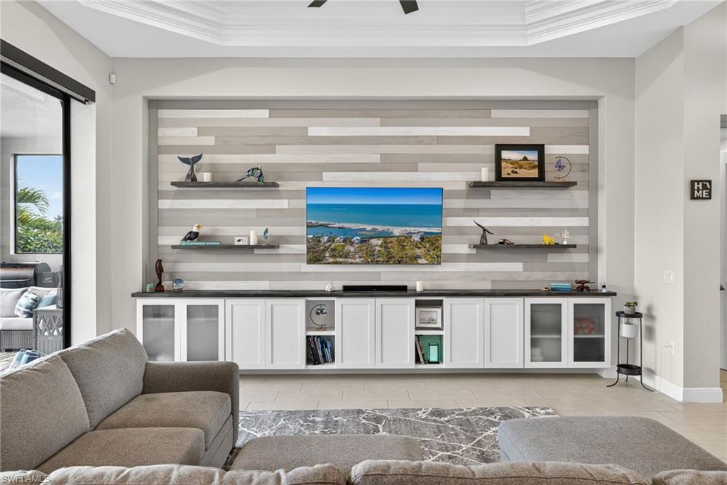 Living room featuring a custom wall with built in cabinets, crown molding, a raised ceiling, and ceiling fan