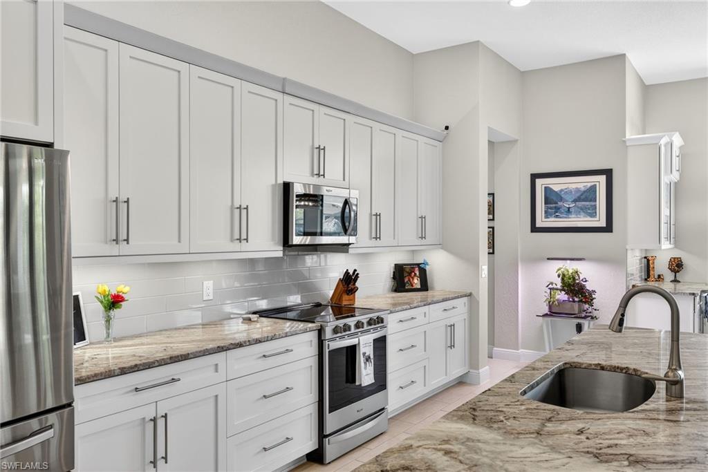 Kitchen featuring stainless steel appliances, white cabinetry, light stone counters, and backsplash