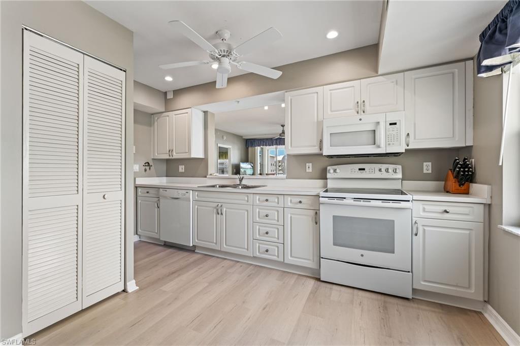 Kitchen with white appliances, light countertops, white cabinetry, a ceiling fan, and light wood finished floors