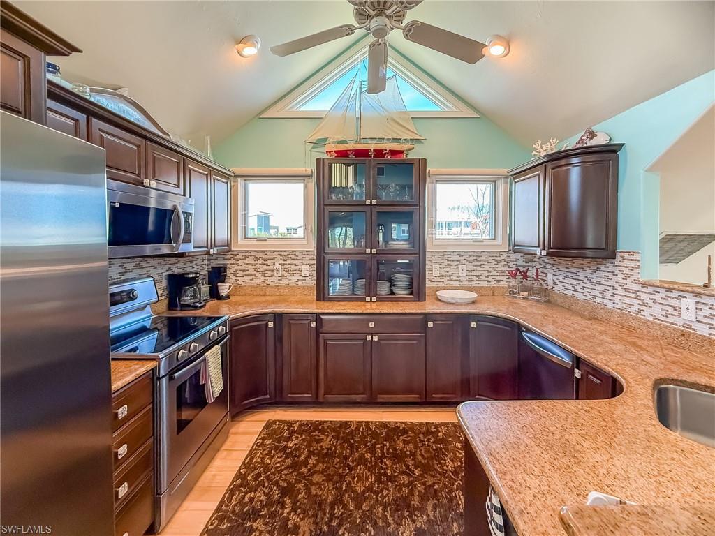 Kitchen featuring light wood-style flooring, appliances with stainless steel finishes, brown cabinets, vaulted ceiling, and backsplash