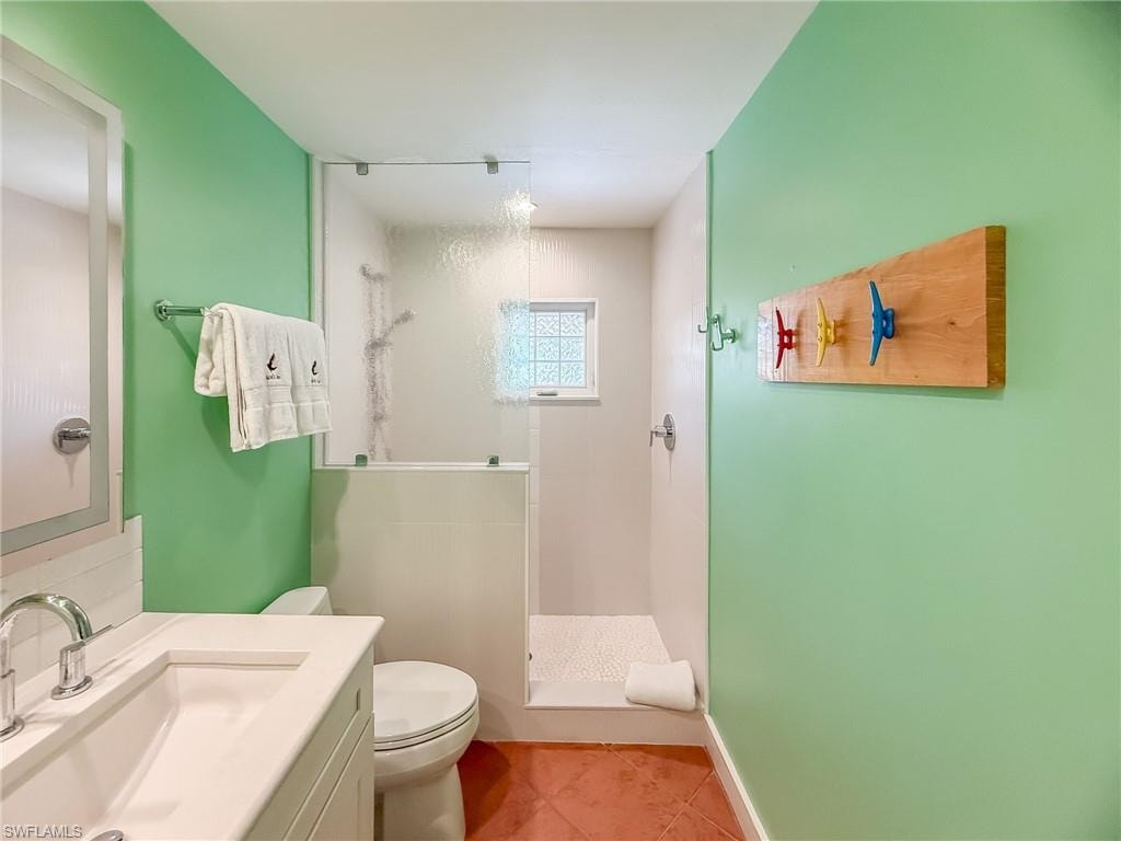 Full bathroom featuring toilet, a stall shower, vanity, baseboards, and tile patterned floors