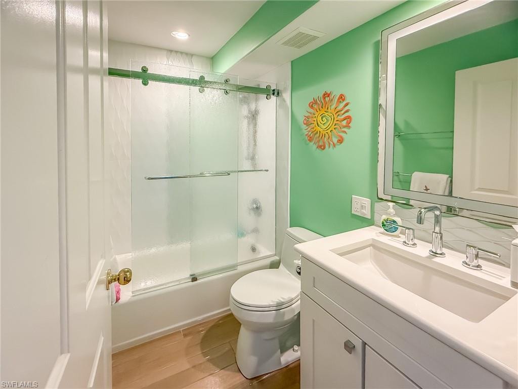 Bathroom with visible vents, toilet, shower / bath combination with glass door, wood finished floors, and vanity