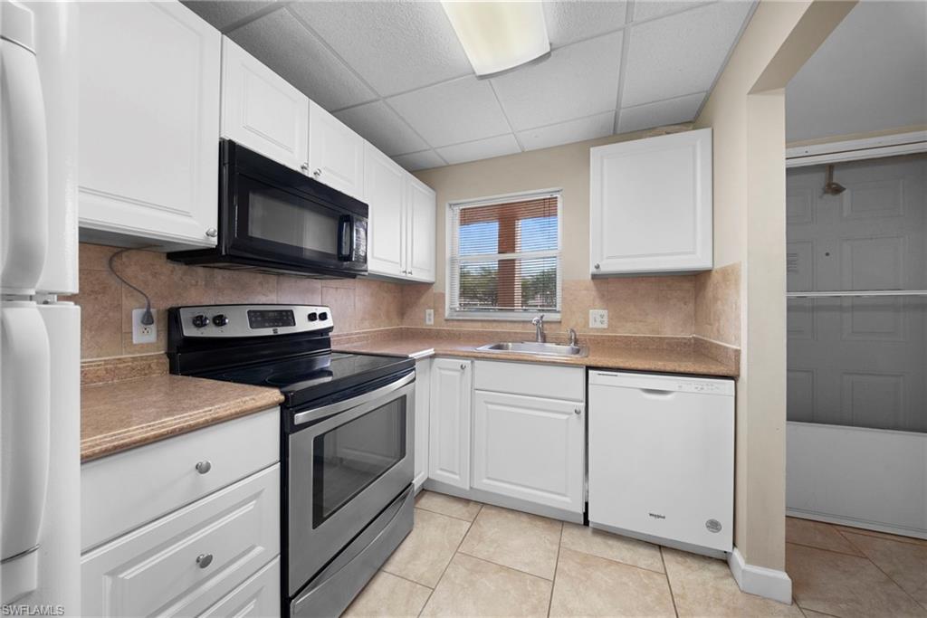 Kitchen featuring stainless steel range with electric cooktop, black microwave, white dishwasher, white cabinets, and a drop ceiling