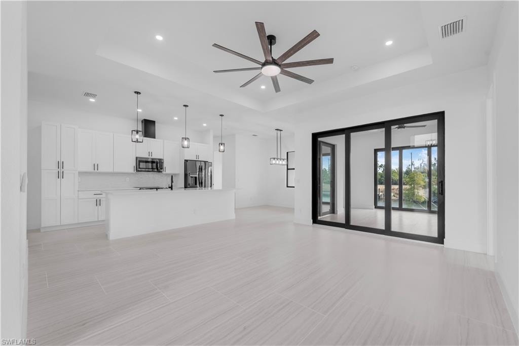 Unfurnished living room featuring ceiling fan, recessed lighting, and a tray ceiling