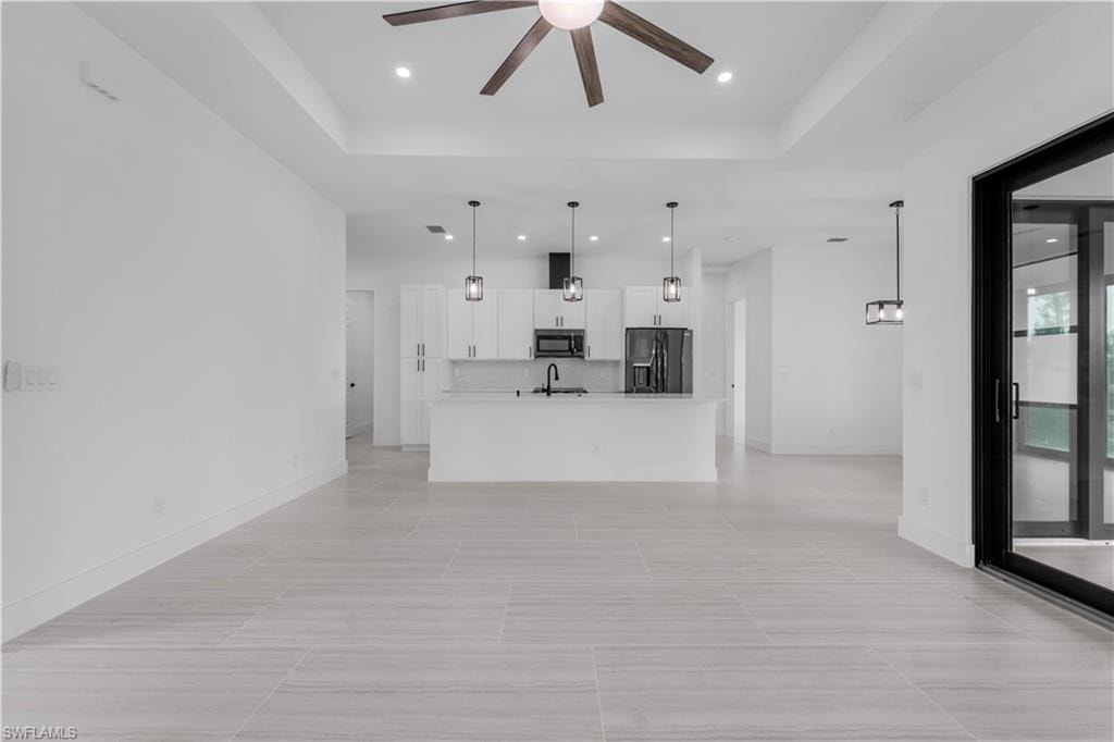 Unfurnished living room featuring a tray ceiling, ceiling fan, and recessed lighting