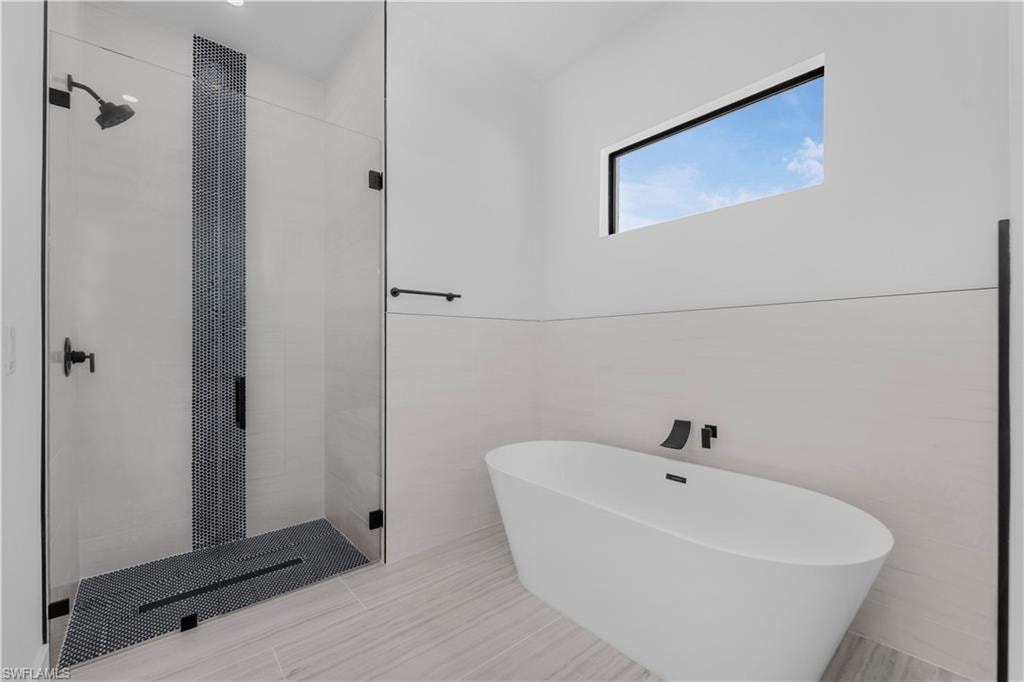 Full Master bath featuring a shower stall, a freestanding tub, and tile walls