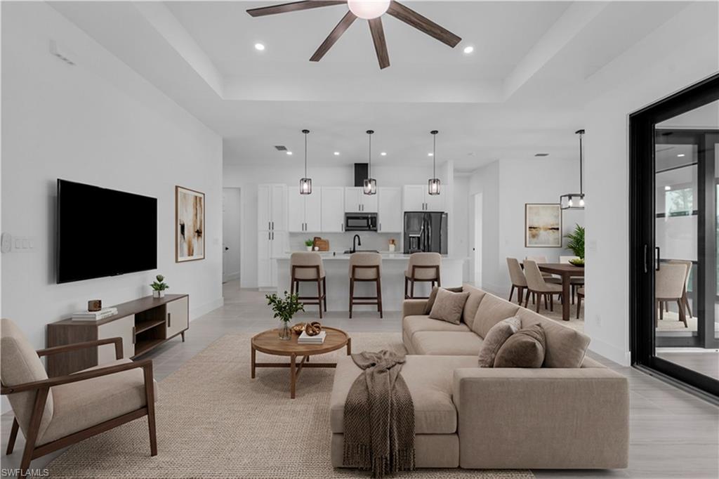 Living room featuring a ceiling fan, recessed lighting, and a high tray ceiling