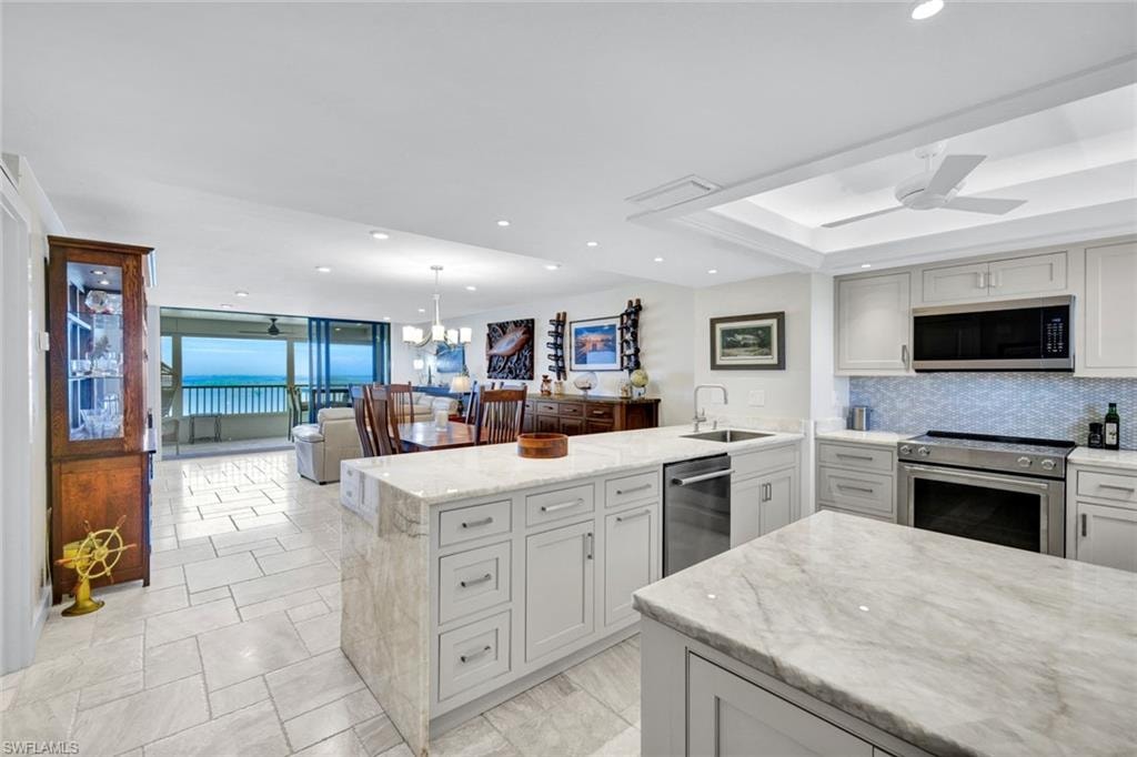 Kitchen featuring light stone counters, a peninsula, a ceiling fan, stainless steel appliances, and a tray ceiling