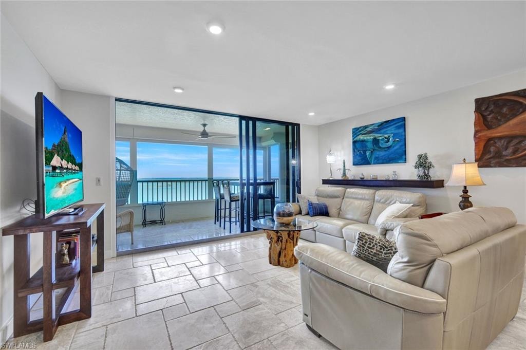 Living room with a ceiling fan, expansive windows, and stone tile flooring
