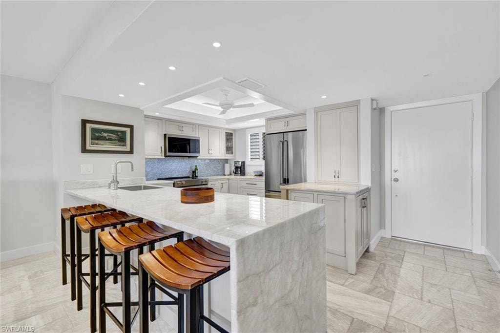 Kitchen with light stone countertops, a kitchen breakfast bar, stainless steel appliances, a peninsula, and a raised ceiling