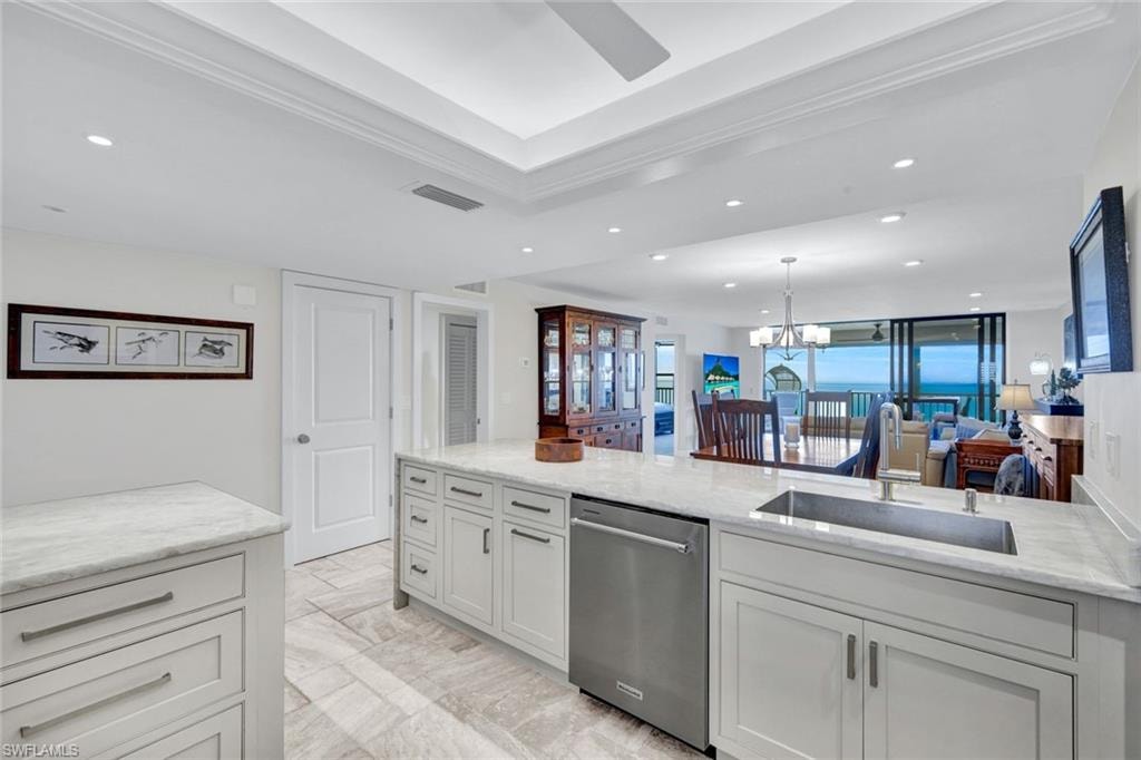 Kitchen with light stone counters, dishwasher, open floor plan, a ceiling fan, and suspended lighting
