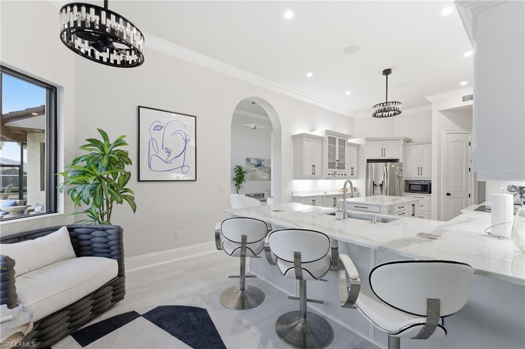 Kitchen featuring arched walkways, light stone counters, white cabinets, a kitchen breakfast bar, and ornamental molding