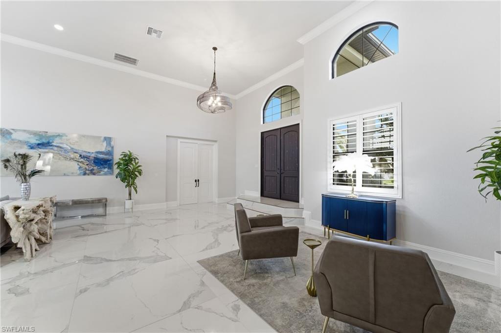 Foyer with a high ceiling, crown molding, and light marble finish flooring