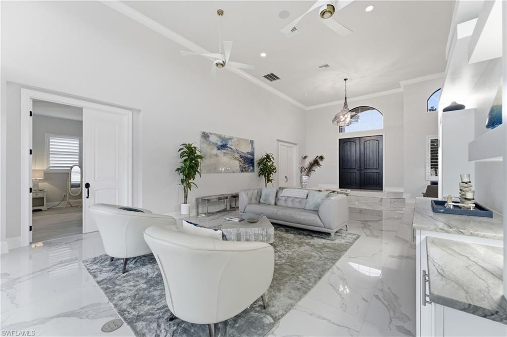 Living area with a high ceiling, healthy amount of natural light, crown molding, ceiling fan, and light marble finish flooring
