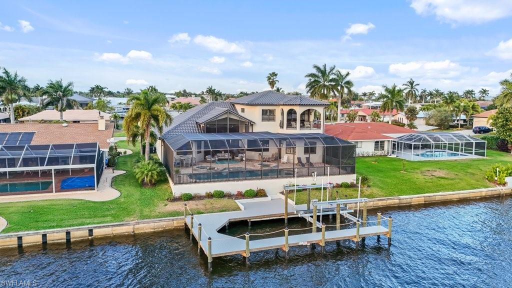 Rear view of property with a water view, an outdoor pool, a sunroom, a yard, and boat lift