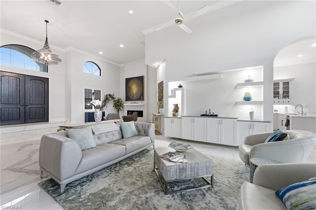 Living area with a high ceiling, crown molding, light marble finish flooring, hanging lights, and ceiling fan