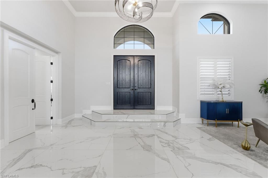 Foyer entrance featuring hanging lights, a high ceiling, crown molding, and light marble finish flooring