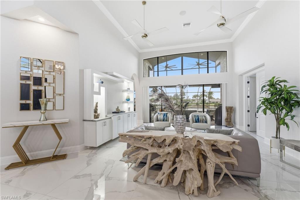 Dining room with ornamental molding, a high ceiling, a ceiling fan, and light marble finish flooring