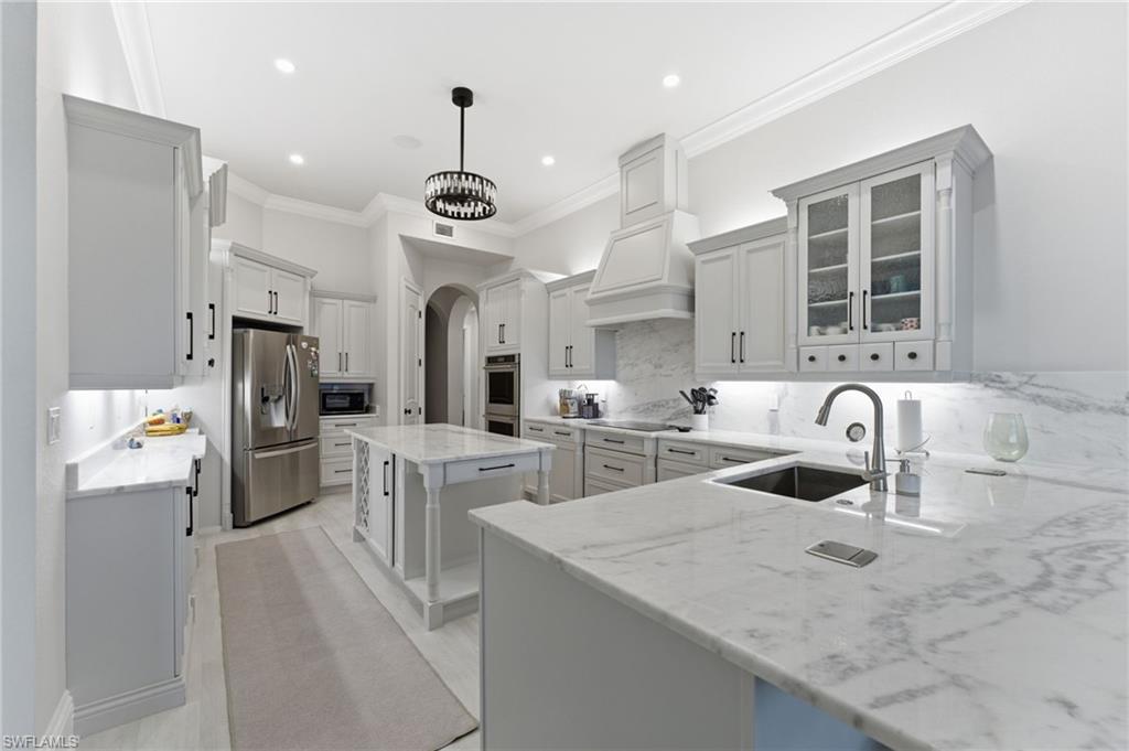 Kitchen featuring glass fronted cabinets, arched walkways, white cabinets, a center island, and stainless steel appliances