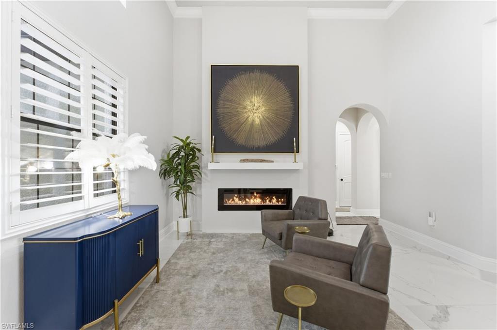 Sitting room featuring a glass covered fireplace, crown molding, marble finish floors, and arched walkways