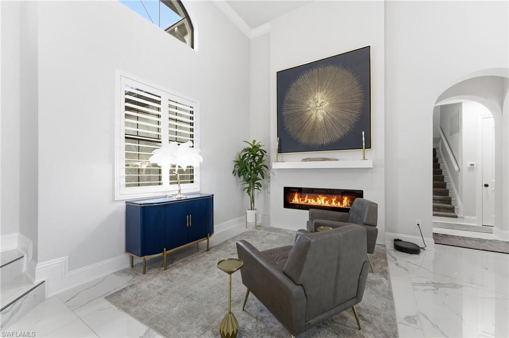 Living room with a high ceiling, arched walkways, a glass covered fireplace, and marble finish floors