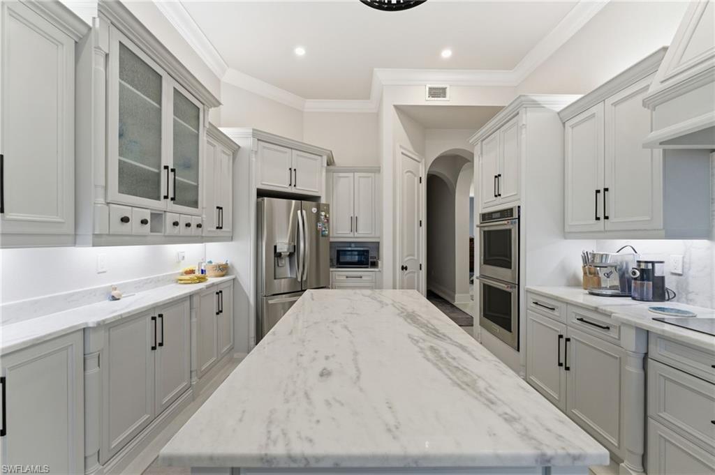 Kitchen featuring light stone counters, arched walkways, glass insert cabinets, stainless steel appliances, and ornamental molding