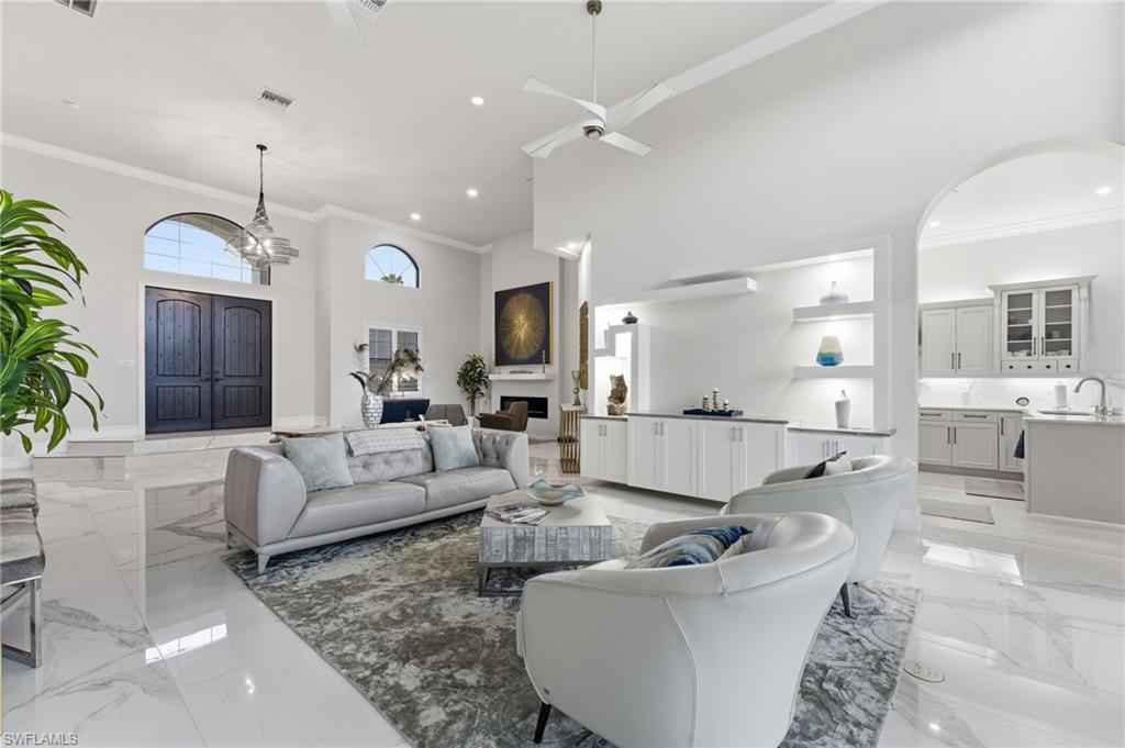 Living room featuring light marble finish flooring, crown molding, a high ceiling, a ceiling fan, and suspended lighting