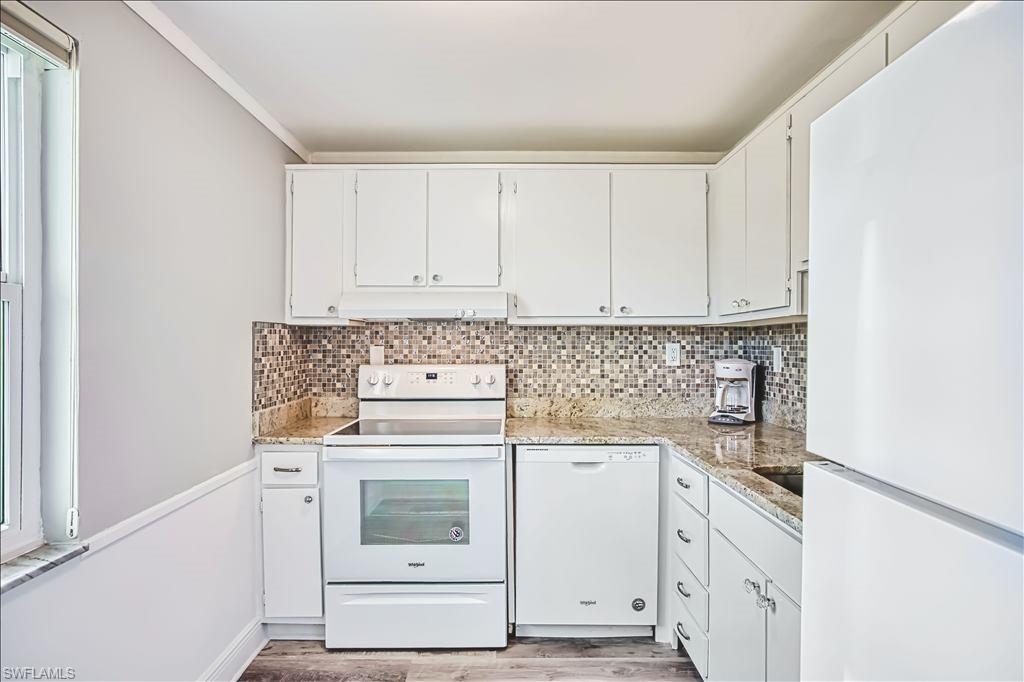 Kitchen featuring white appliances, white cabinets, light stone countertops, light wood-style flooring, and ornamental molding