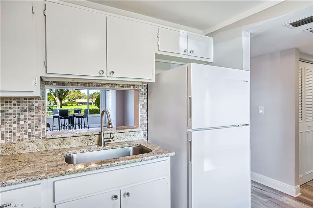 Kitchen with freestanding refrigerator, light stone countertops, white cabinets, and light wood-type flooring