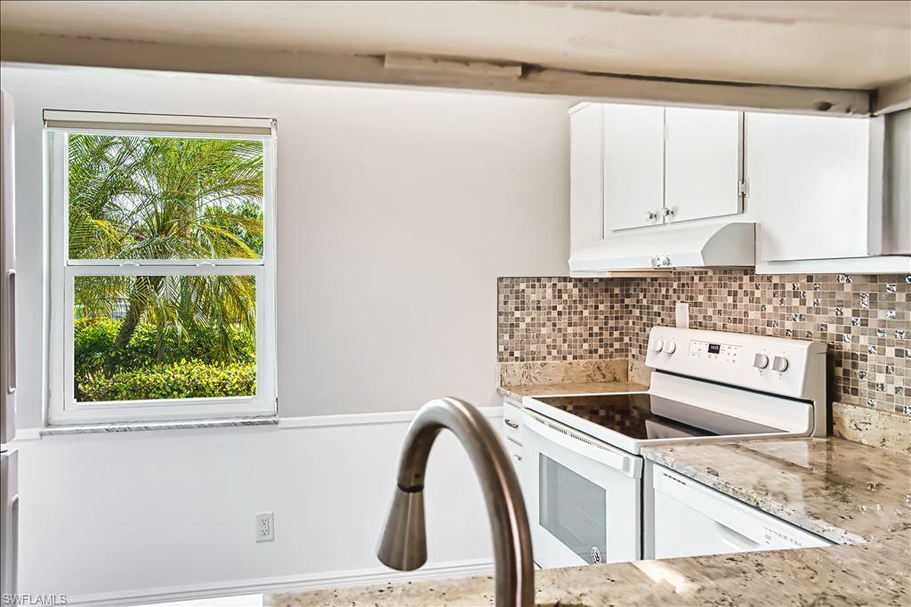 Kitchen featuring electric range, white cabinets, light stone counters, and backsplash