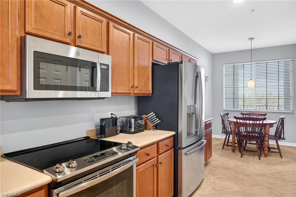 Kitchen featuring stainless steel appliances, light countertops, wood finish cabinetry, hanging light fixtures, and light tile patterned floors