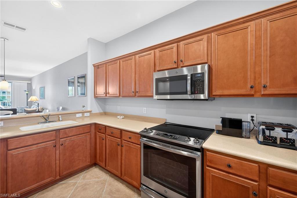 Kitchen featuring stainless steel appliances, wood finish cabinets, light countertops, and hanging light fixtures