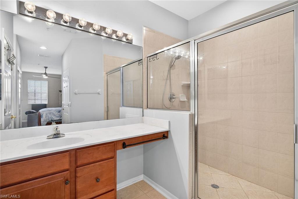 Ensuite bathroom featuring a stall shower, vanity, light tile patterned flooring, and ceiling fan