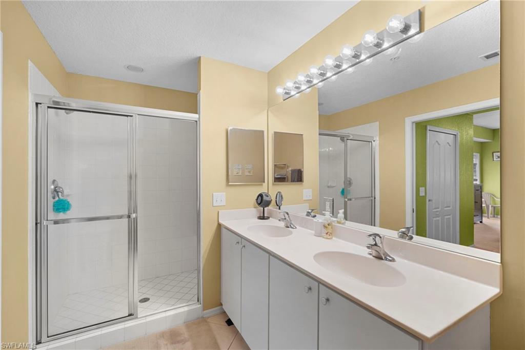 Full bath featuring double vanity, a shower stall, light tile patterned flooring, and a textured ceiling