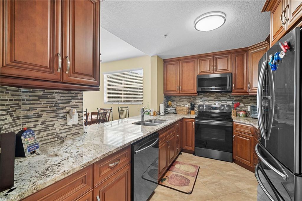 Kitchen featuring stainless steel appliances, light stone counters, wood finish cabinets, decorative backsplash, and a textured ceiling