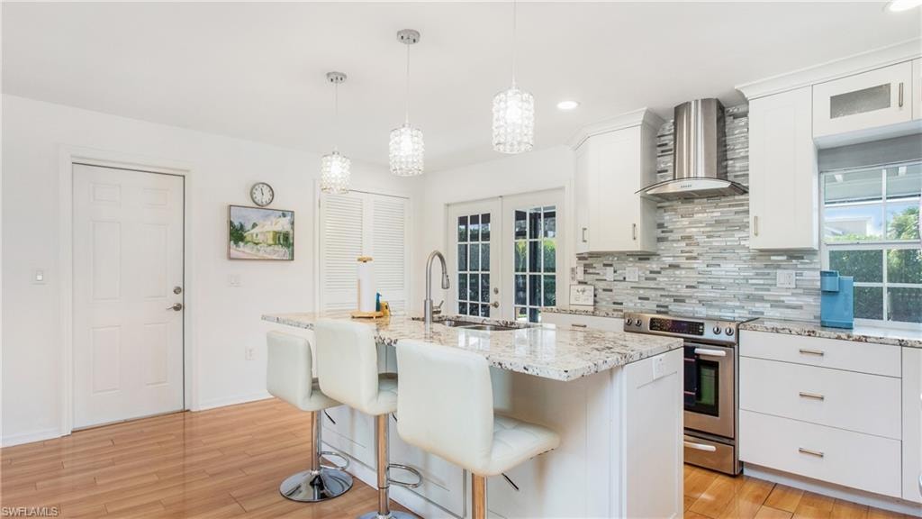 Kitchen featuring white cabinets, stainless steel range with electric cooktop, an island with sink, french doors, and light stone counters
