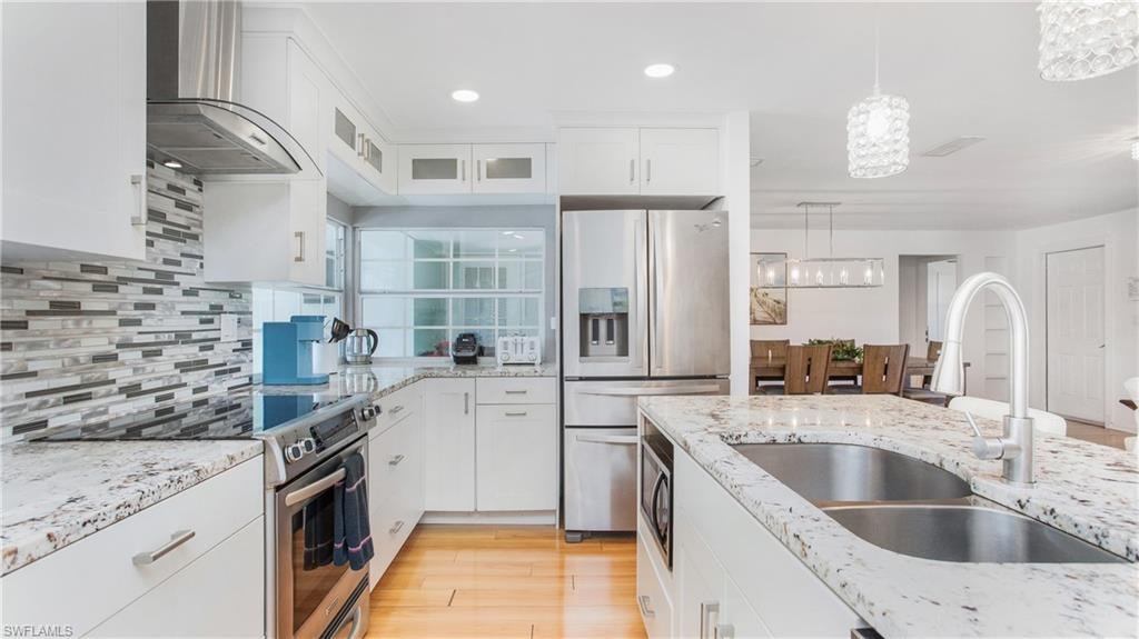 Kitchen with white cabinetry, stainless steel appliances, light stone countertops, glass fronted cabinets, and light wood finished floors