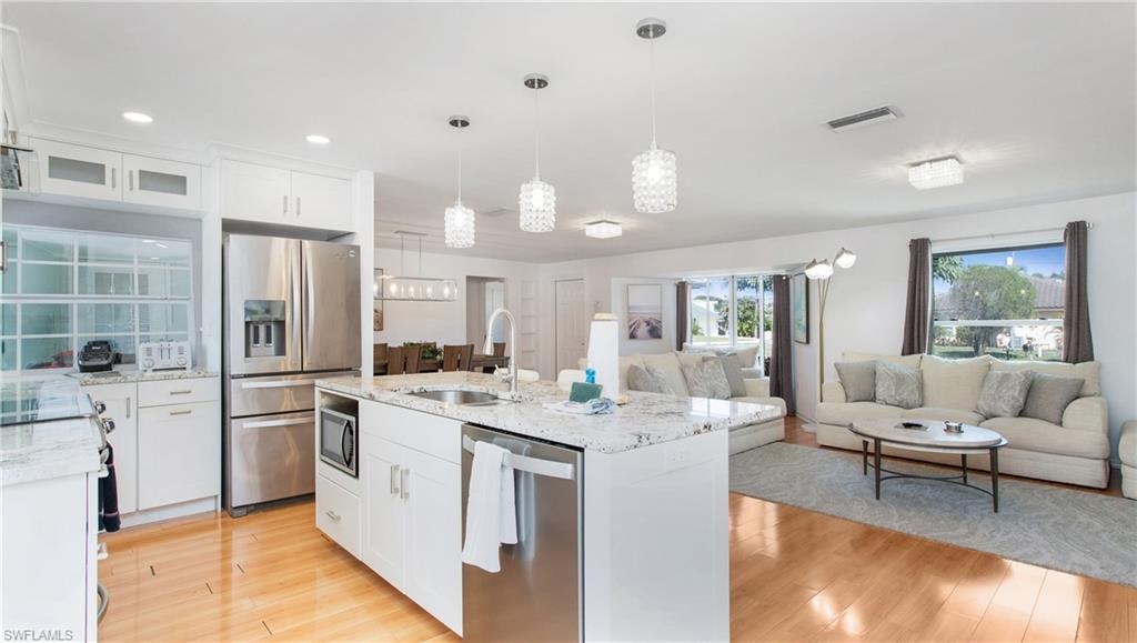 Kitchen featuring white cabinetry, open floor plan, stainless steel appliances, light stone countertops, and glass insert cabinets